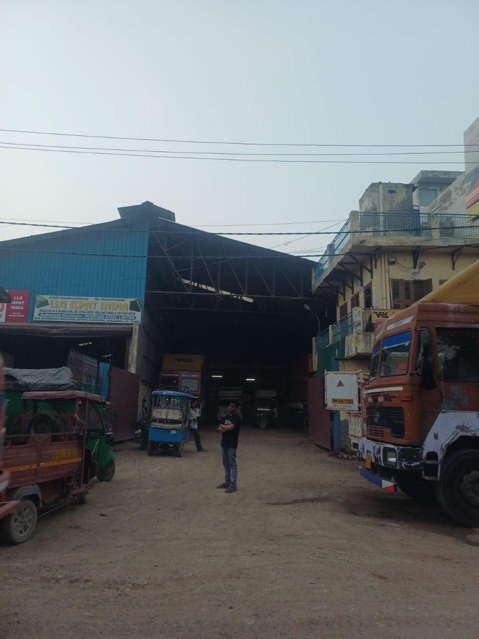 Krishna standing in a logistics yard with trucks and a warehouse shed